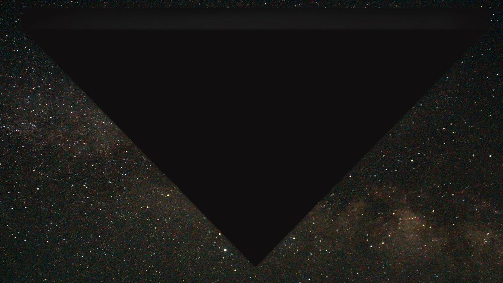 Triângulo negro enorme ocupando a parte de cima de um céu estrelado, com a Via Láctea visível nas laterais.