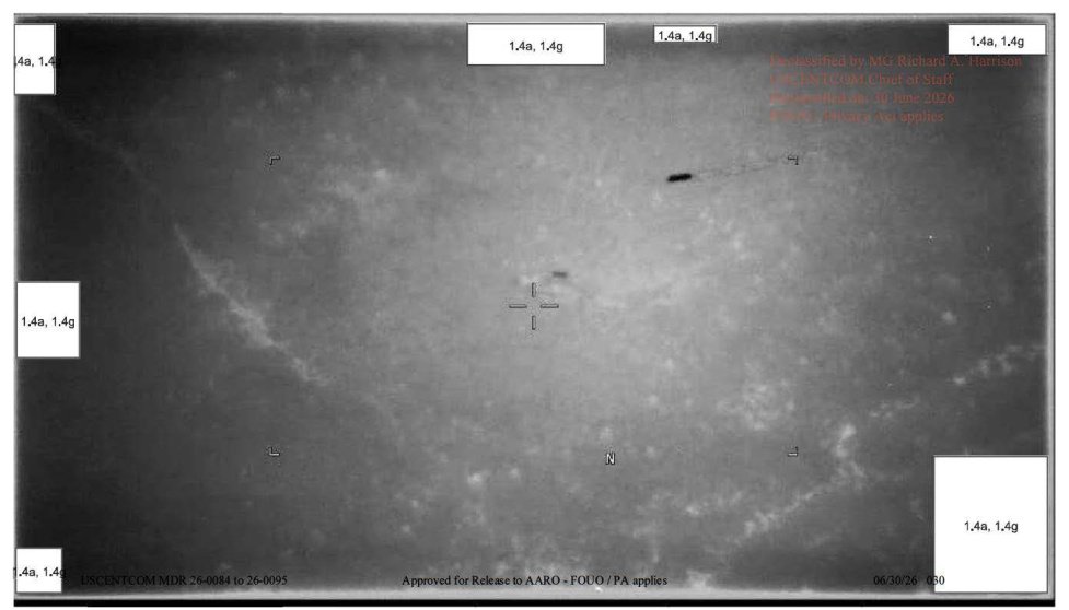 Imagem de sensor em tons de cinza com retículo de mira e, no alto, uma pequena forma escura alongada seguida de um rastro fino.
