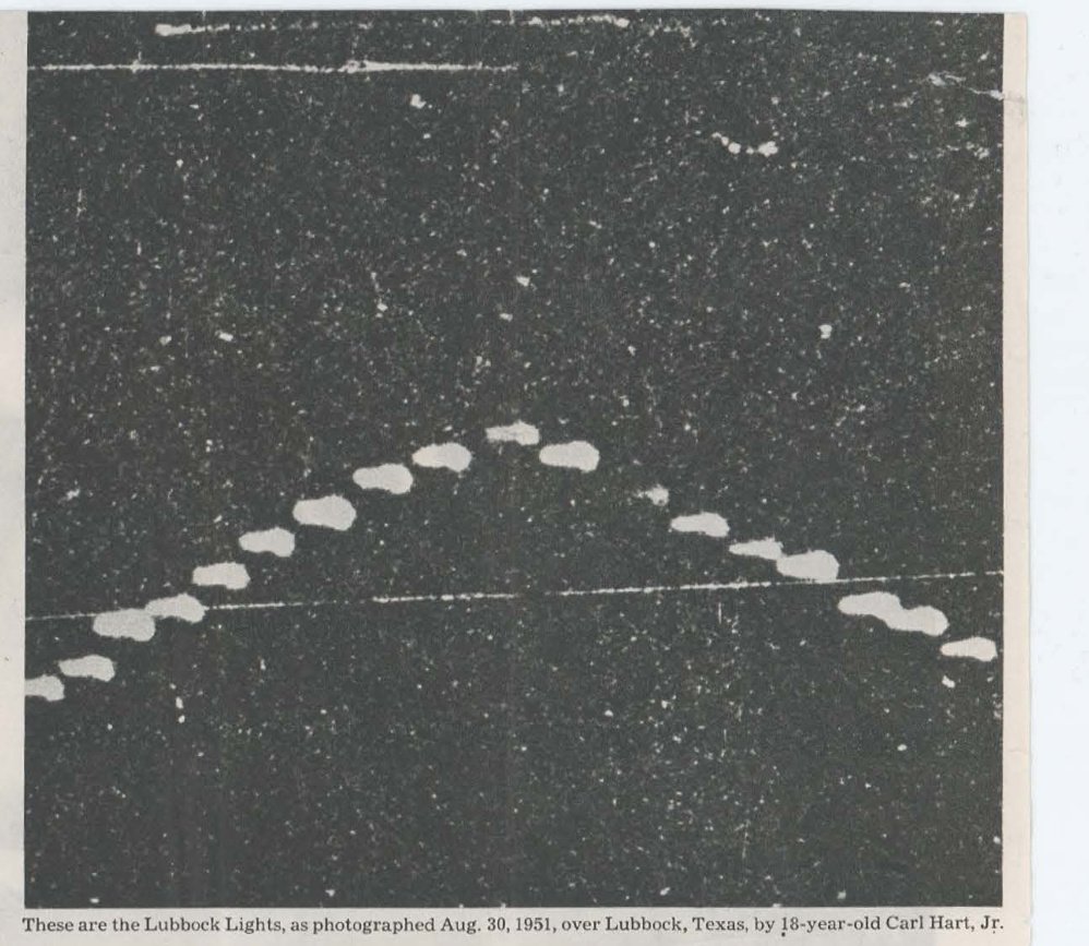 Fotografia noturna em preto e branco com cerca de vinte manchas claras dispostas num arco em forma de V invertido, com legenda em inglês na base.