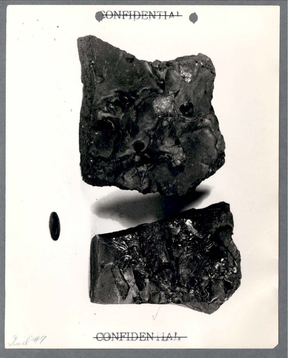 Fotografia em preto e branco de dois blocos escuros de aspecto derretido, com bolhas e cavidades na superfície.