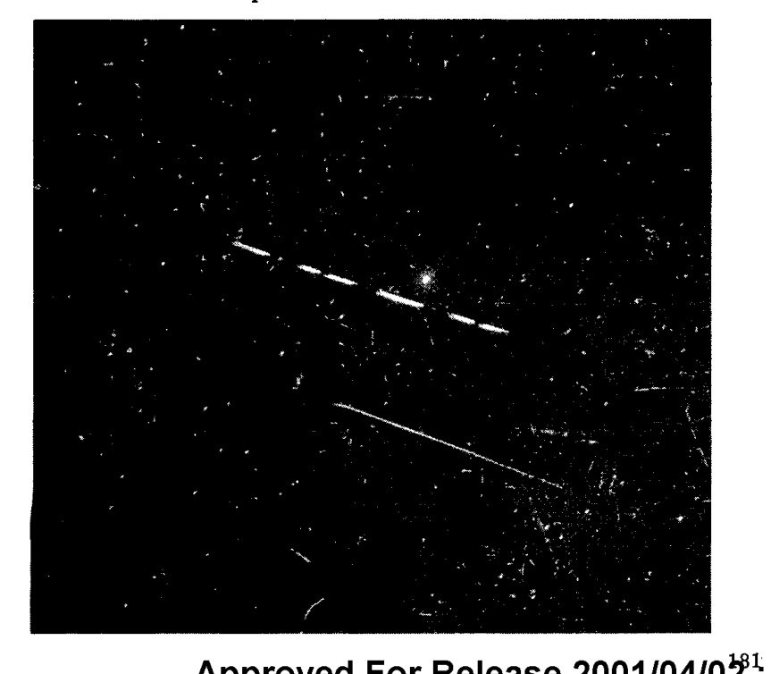 Fotografia de céu noturno com muitas estrelas, uma linha branca tracejada na diagonal e um traço fino contínuo abaixo dela.