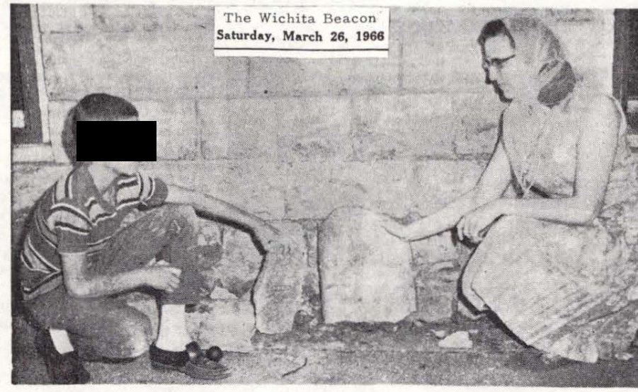 Fotografia de jornal com um menino e uma mulher agachados diante de pedaços de concreto quebrado junto a uma parede de pedra; os olhos do menino estão cobertos por uma tarja preta.